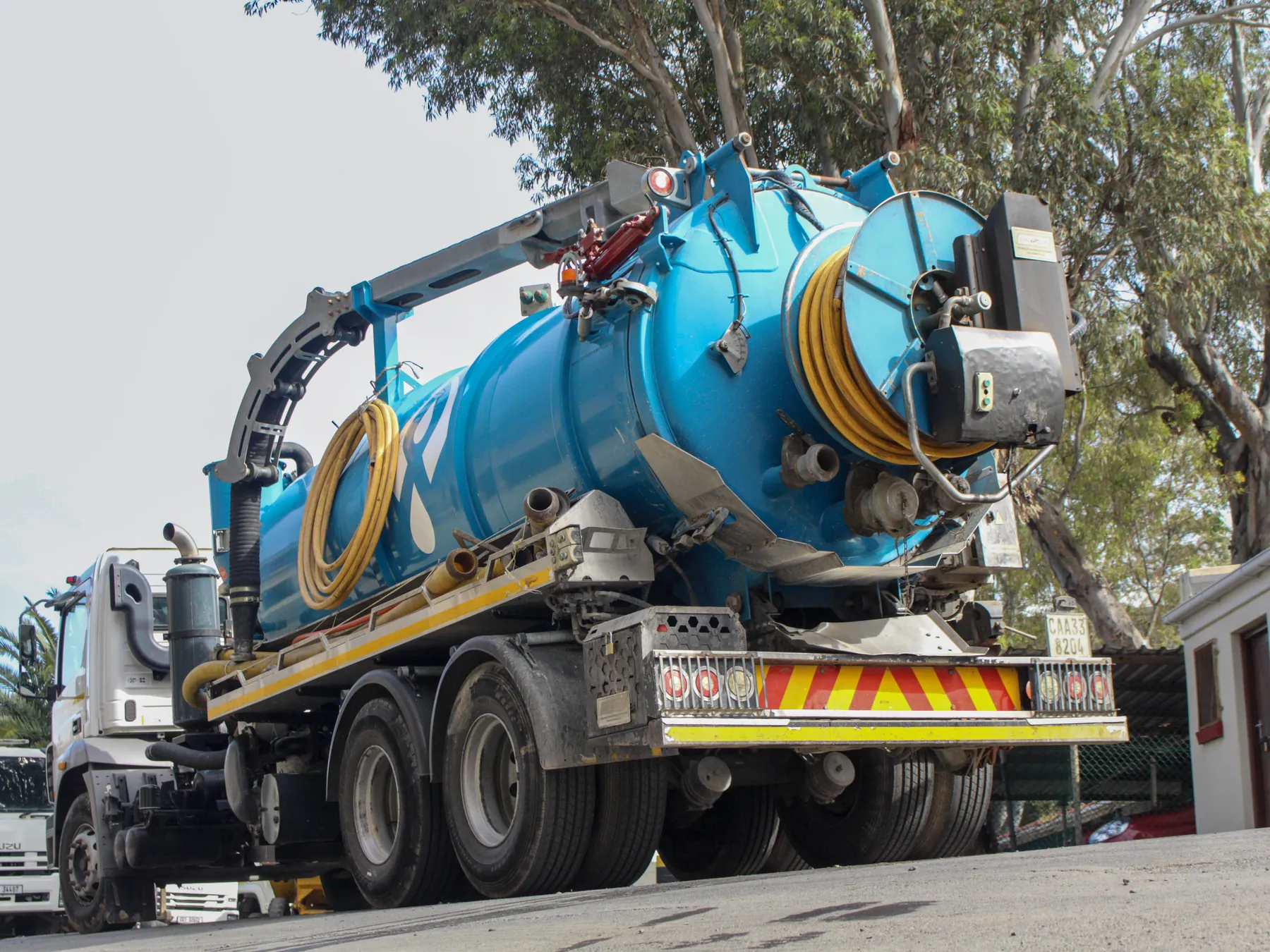 Blue combination vacuum and jetting truck parked on a tree-lined street
