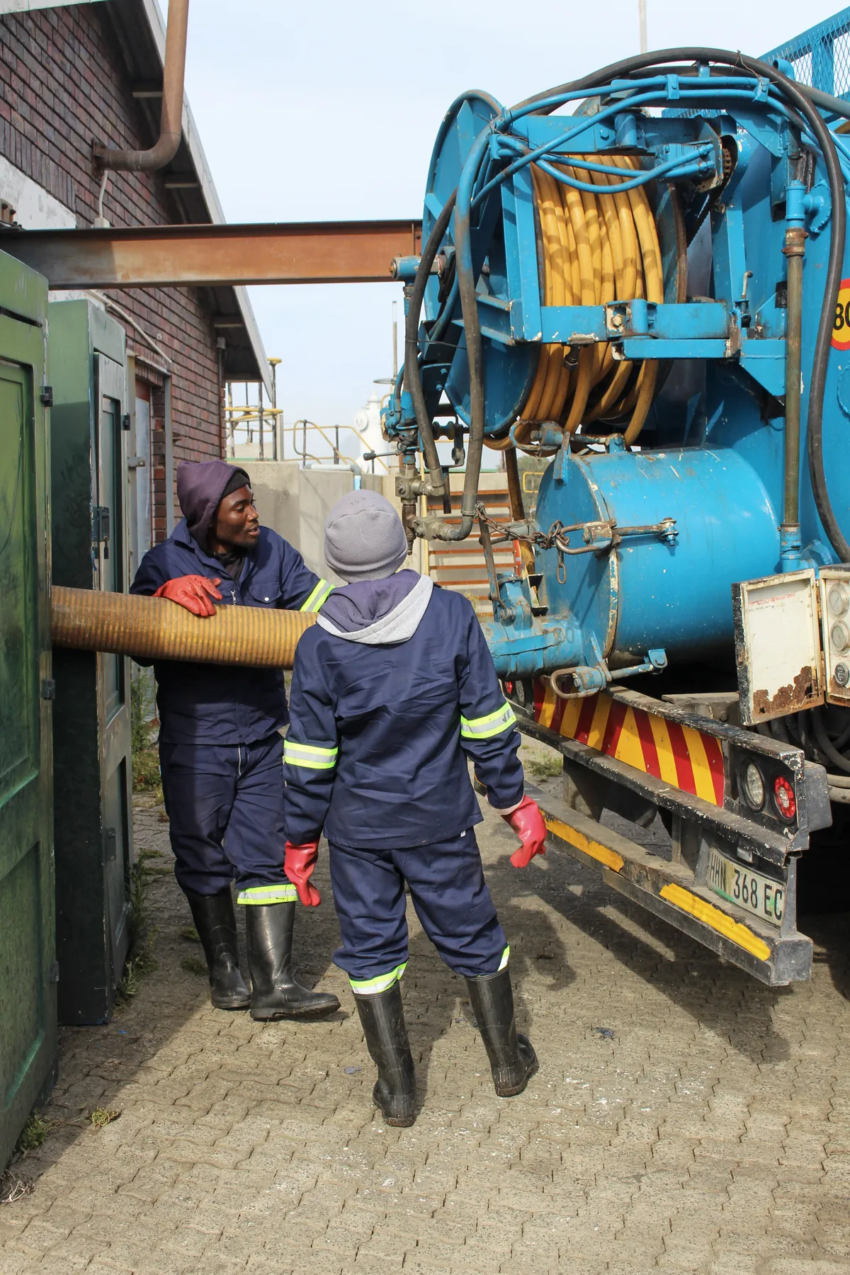 Two crew members handling a suction hose beside a combination truck
