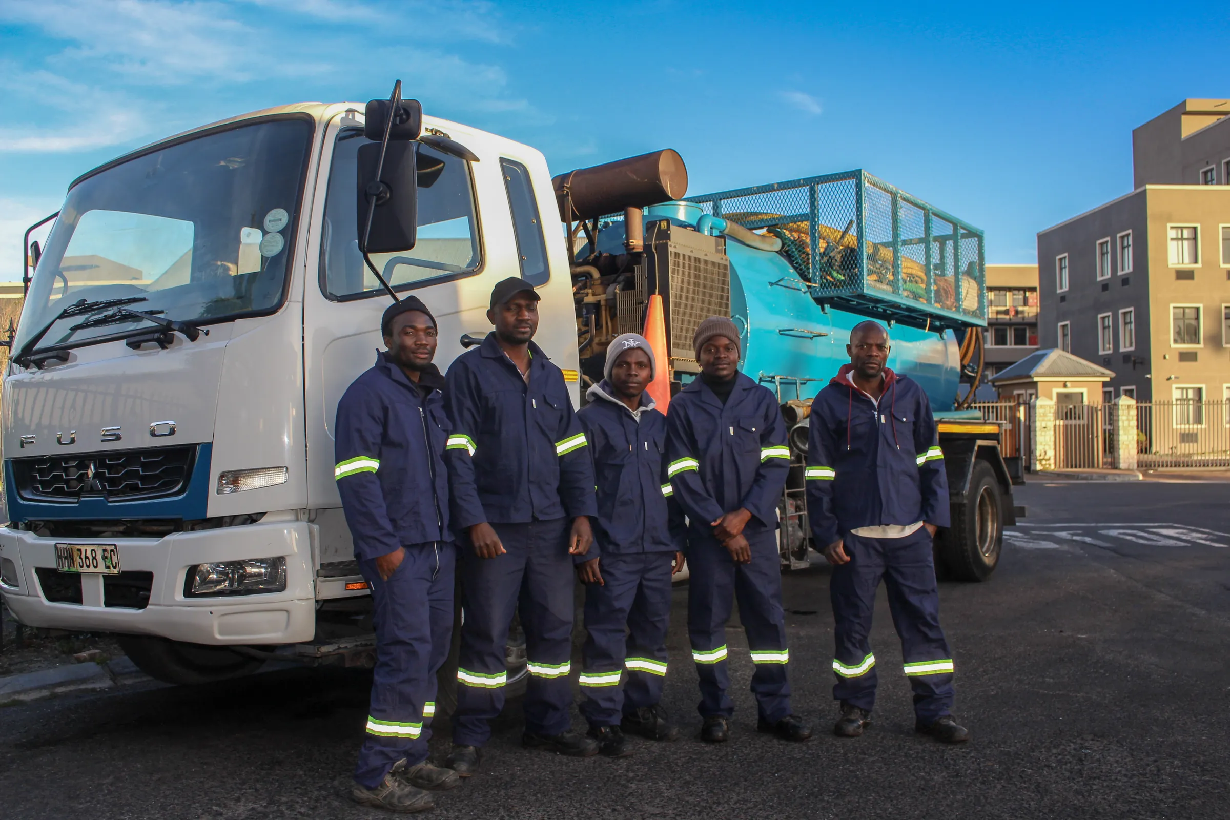 Five Ramatini crew members in navy overalls standing in front of a vacuum tanker