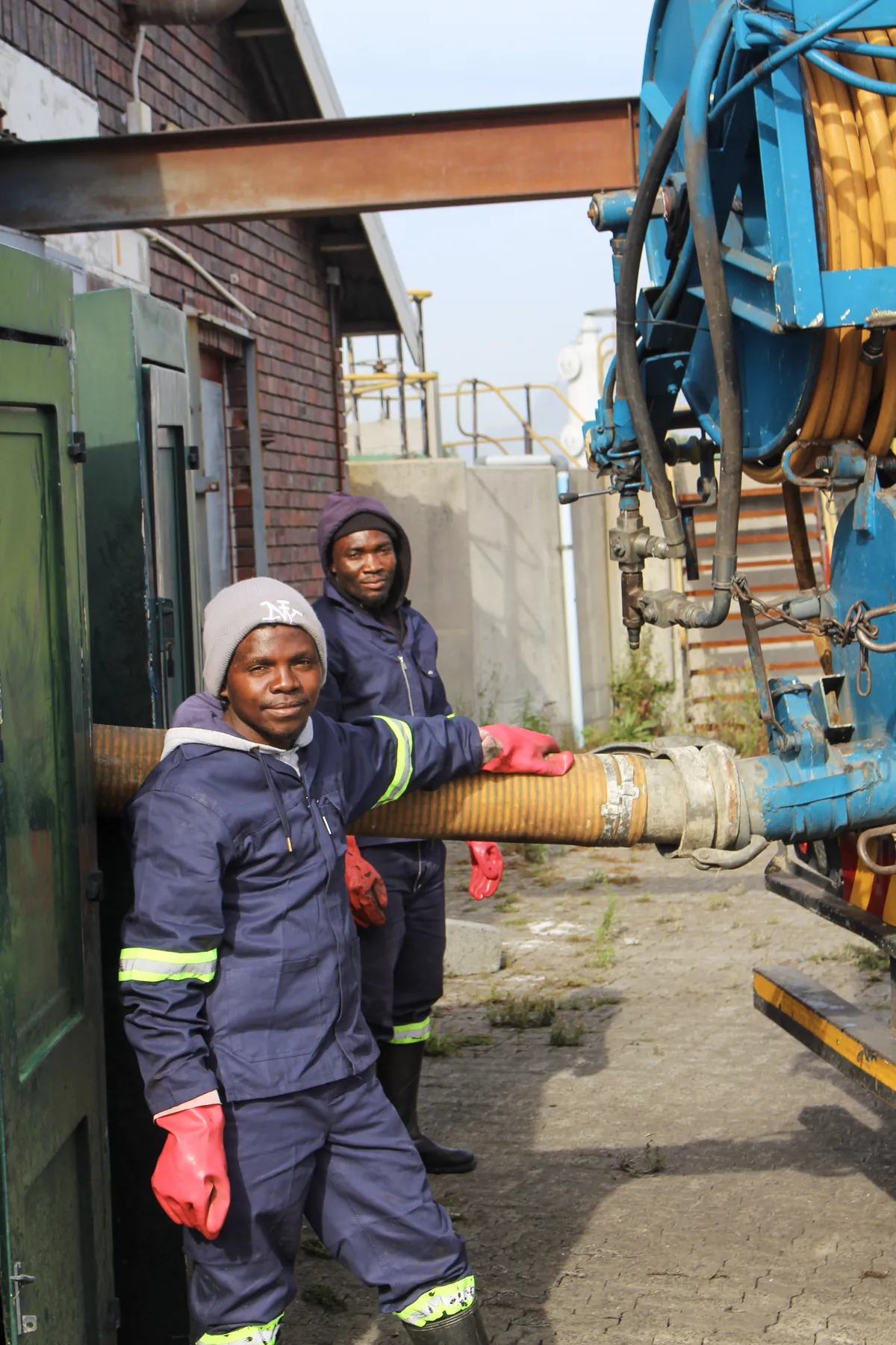 Smiling crew member holding the suction hose beside a tanker